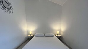 A small, minimalist bedroom with a single bed, two bedside tables with lamps, and a wall decoration.