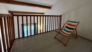 A balcony with a wooden railing, a single beach chair, and a view of a building through the railing.