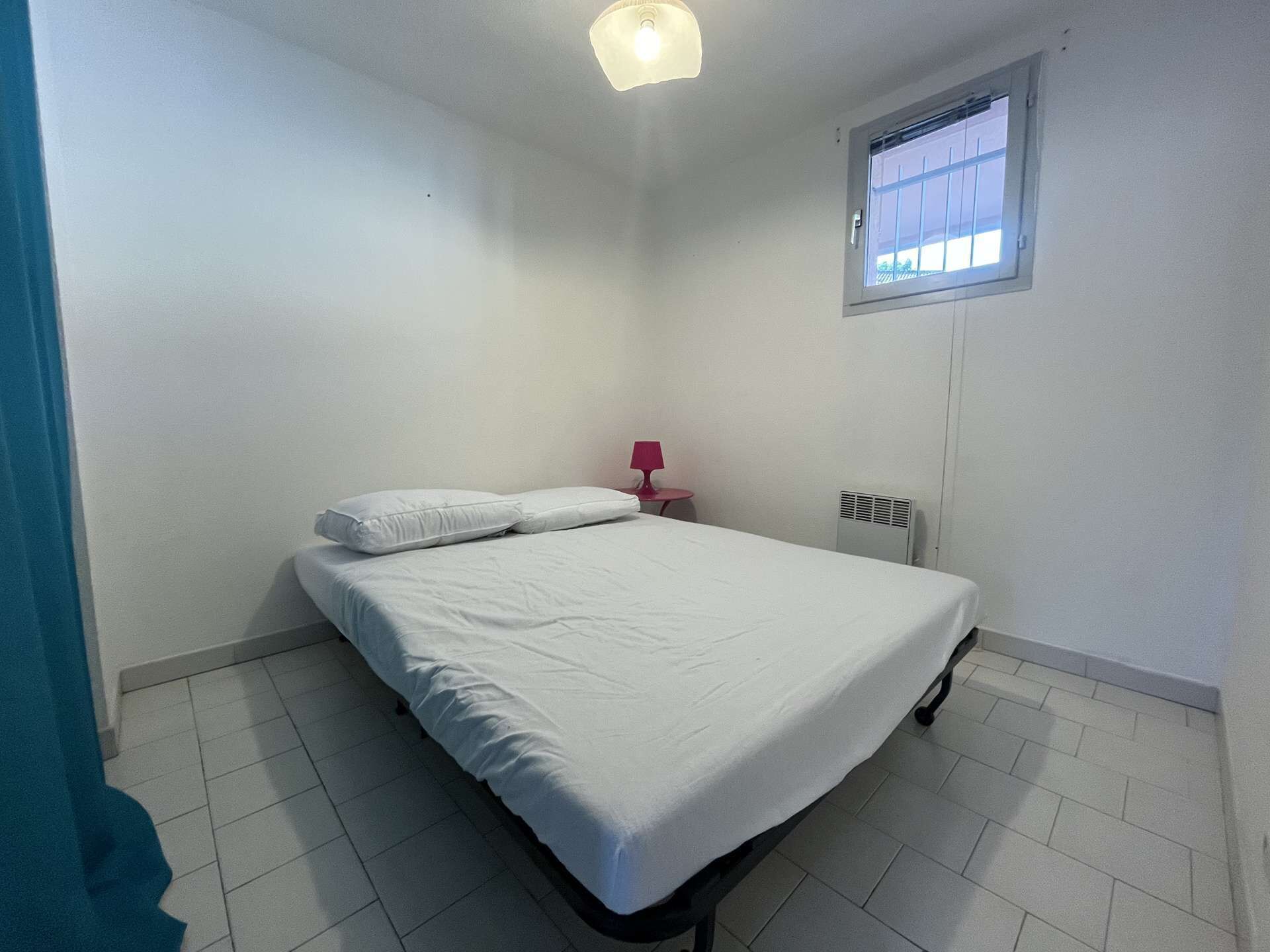 Et lille, rent værelse med en seng, et vindue og en varmeblæser.