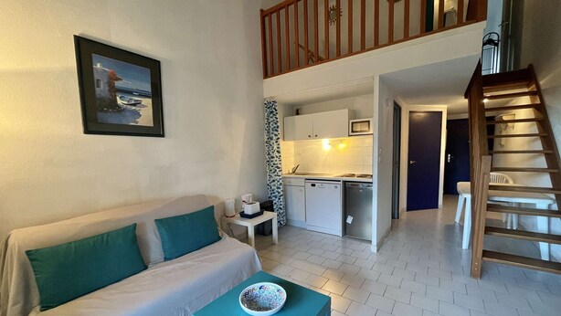 A living room with a sofa, a small table with a bowl, a kitchen area with a microwave, and a staircase leading to an upper level.