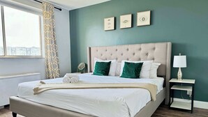 A neatly made bed with pillows and a blanket, a bedside table with a lamp, and a window with curtains. - Stylish 2BR Apartment with City View (Atlanta)