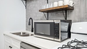 A kitchen with a stainless steel microwave, a gas stove, a sink, and a shelf with cups and a plant. - Stylish 2BR Apartment with City View (Atlanta)