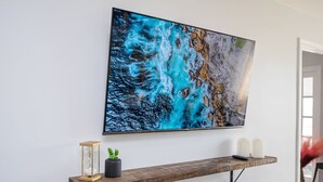 A wall-mounted painting of a blue and white abstract landscape, a wooden shelf with a potted plant, candles, and a remote control. - Stylish 2BR Apartment with City View (Atlanta)
