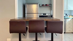 Een compacte keuken met een geïntegreerde koelkast en oven, een klein aanrecht en een eethoek met twee krukken.