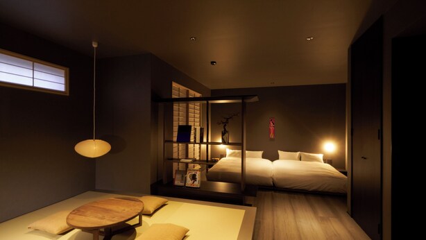 Quarto moderno com cama, mesas de cabeceira, piso de madeira e janela com persianas.