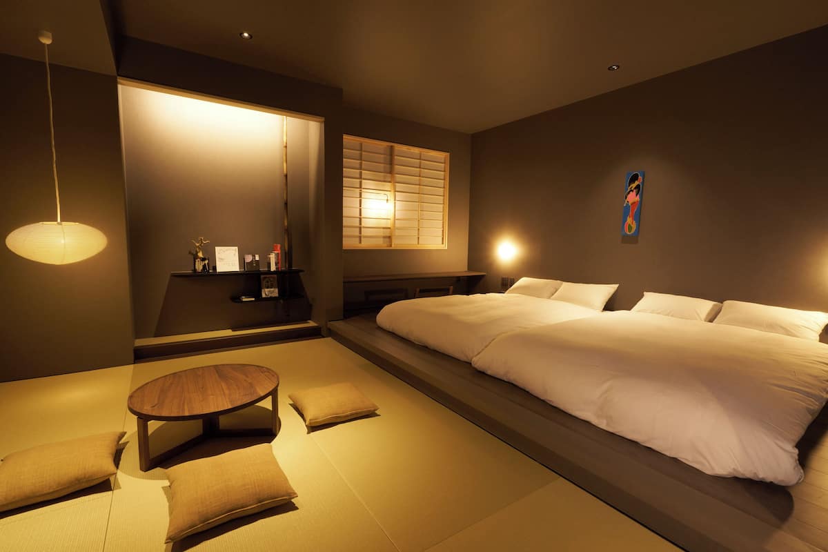 Una habitación de hotel moderna con una cama grande, una pequeña mesa de madera y una zona de estar con esteras de tatami.