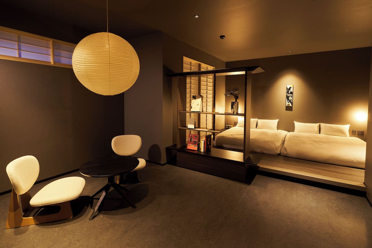 Una habitación de hotel moderna con una cama, una pequeña mesa con sillas, un gran farol de papel y una puerta corredera que da al baño.