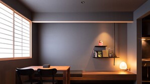 Quarto moderno com mesa e cadeiras de madeira, prateleira embutida com livros e uma luminária.