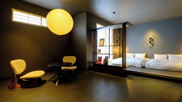 A modern bedroom with a bed, two chairs, a small table, a bookshelf, and a large window.