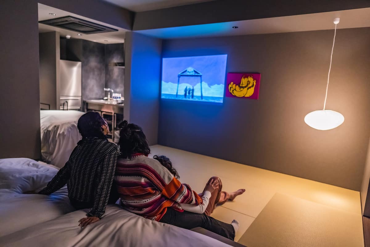 Una habitación de hotel moderna con una cama, una pantalla de televisión y un proyector de pared.