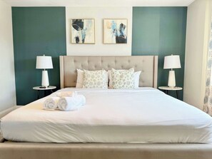 Quarto de hotel com uma cama grande, duas mesas de cabeceira com abajures, uma cabeceira estofada e obras de arte abstratas nas paredes.