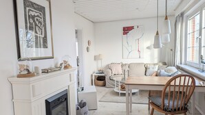 A living room with a fireplace, a dining table, a sofa, and a window with curtains. - Hygge Frisian House by the Sea with Private Garden and Terrace (Nordstrand)