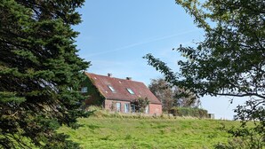 A house with a sloped roof, surrounded by a grassy field and trees. - Hygge Frisian House by the Sea with Private Garden and Terrace (Nordstrand)