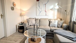 A living room with a sofa, a glass coffee table, a lamp, and a painting on the wall. - Hygge Frisian House by the Sea with Private Garden and Terrace (Nordstrand)