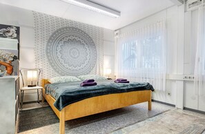 A bedroom with a bed, a chair, a lamp, a tapestry, and a window with curtains. - Holiday Home 'Wohncontainer Derdak' with Private Terrace, Wi-Fi and Air Conditioning (Boizenburg)