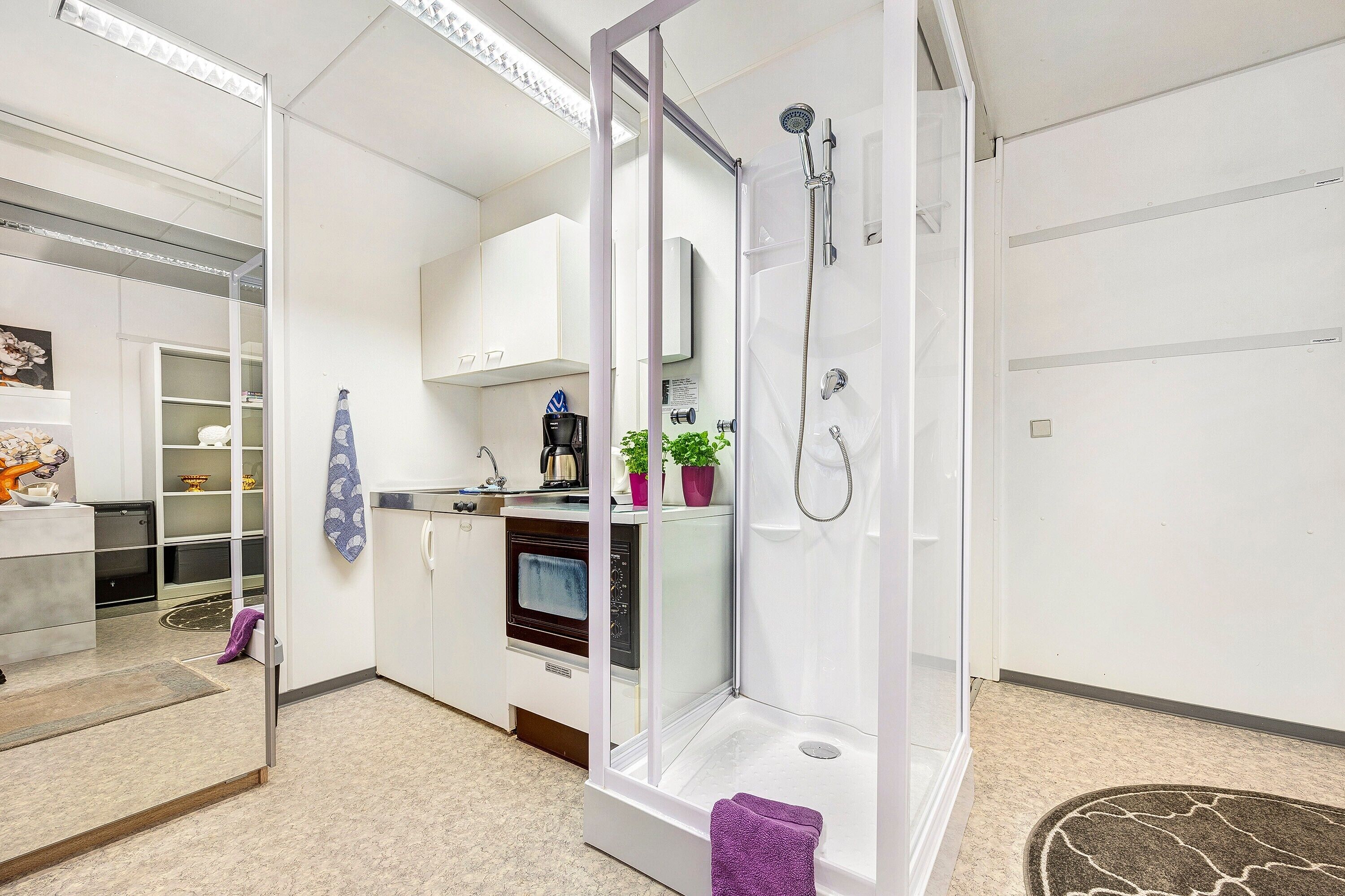 Ein modernes Badezimmer mit einer Duschkabine aus Glas, einem weißen Waschbecken und einer Arbeitsplatte mit einer Kaffeemaschine.