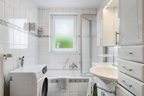A modern bathroom with a built-in washer, a bathtub, a shower, and a sink.