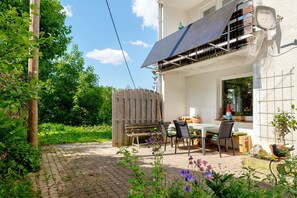 Eine Terrasse mit Tisch und Stühlen, ein Holzzaun und ein Solarmodul am Gebäude.
