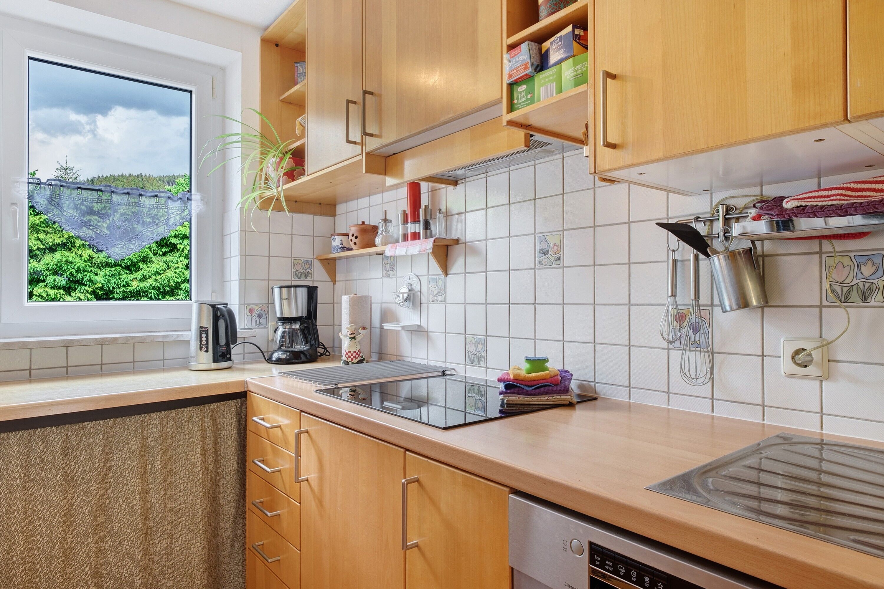 A kitchen with wooden cabinets, a window with a view, a coffee maker, and a dishwasher.