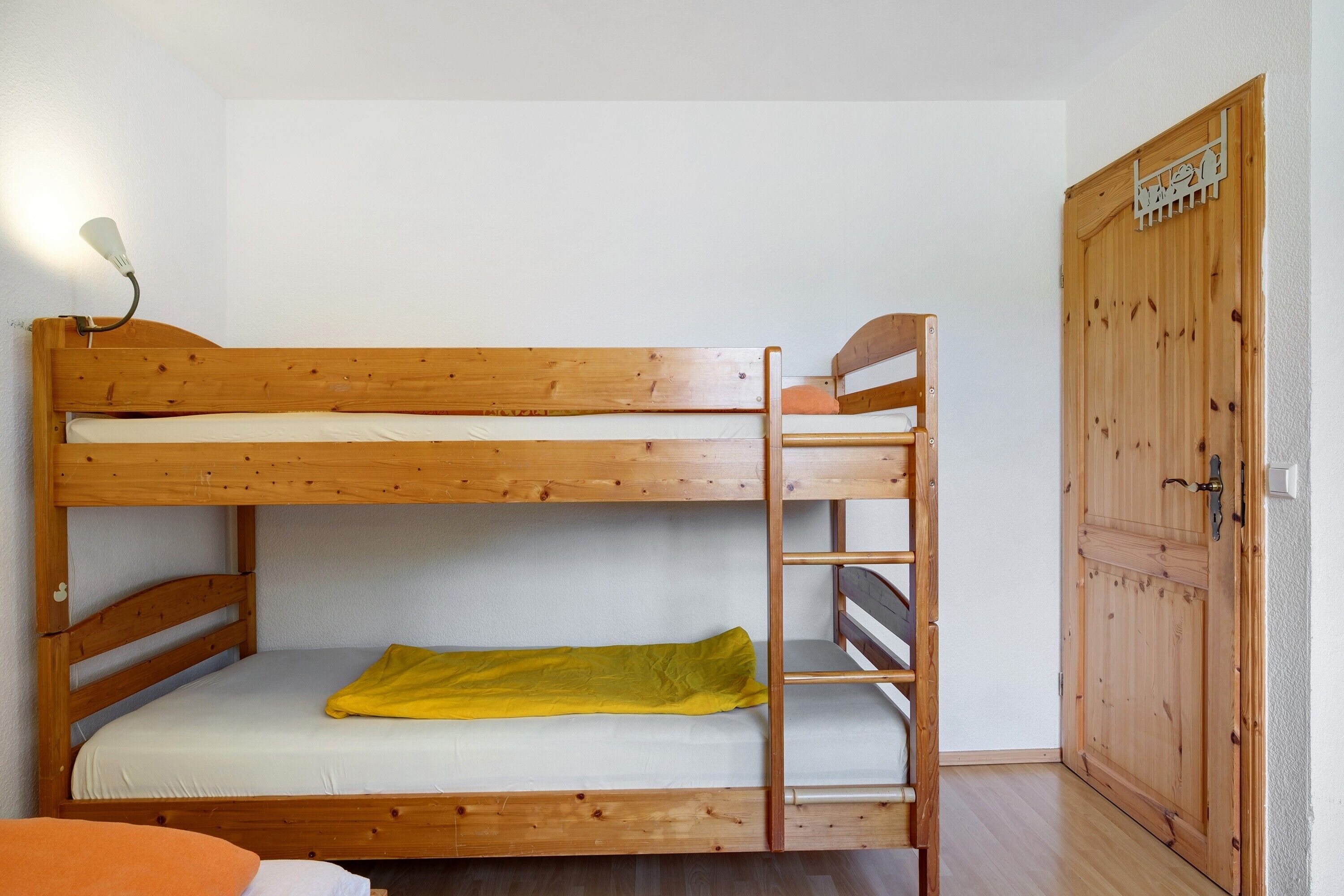 Un lit superposé avec une échelle, une porte en bois et un luminaire.