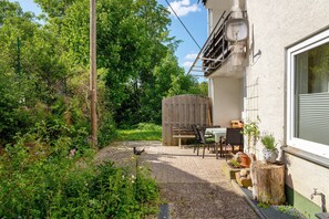 A patio with a table and chairs, a wooden fence, and a window with a shutter.