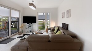 Un salon moderne avec un canapé, un téléviseur à écran plat et une porte-fenêtre coulissante donnant sur un espace extérieur.
