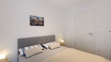 Un dormitorio con cama, mesitas de noche, una puerta y un cuadro colgado en la pared.
