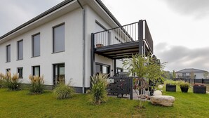 Une maison moderne à deux étages, dotée d’un balcon, d’une pelouse bien entretenue et de plantes en pot.