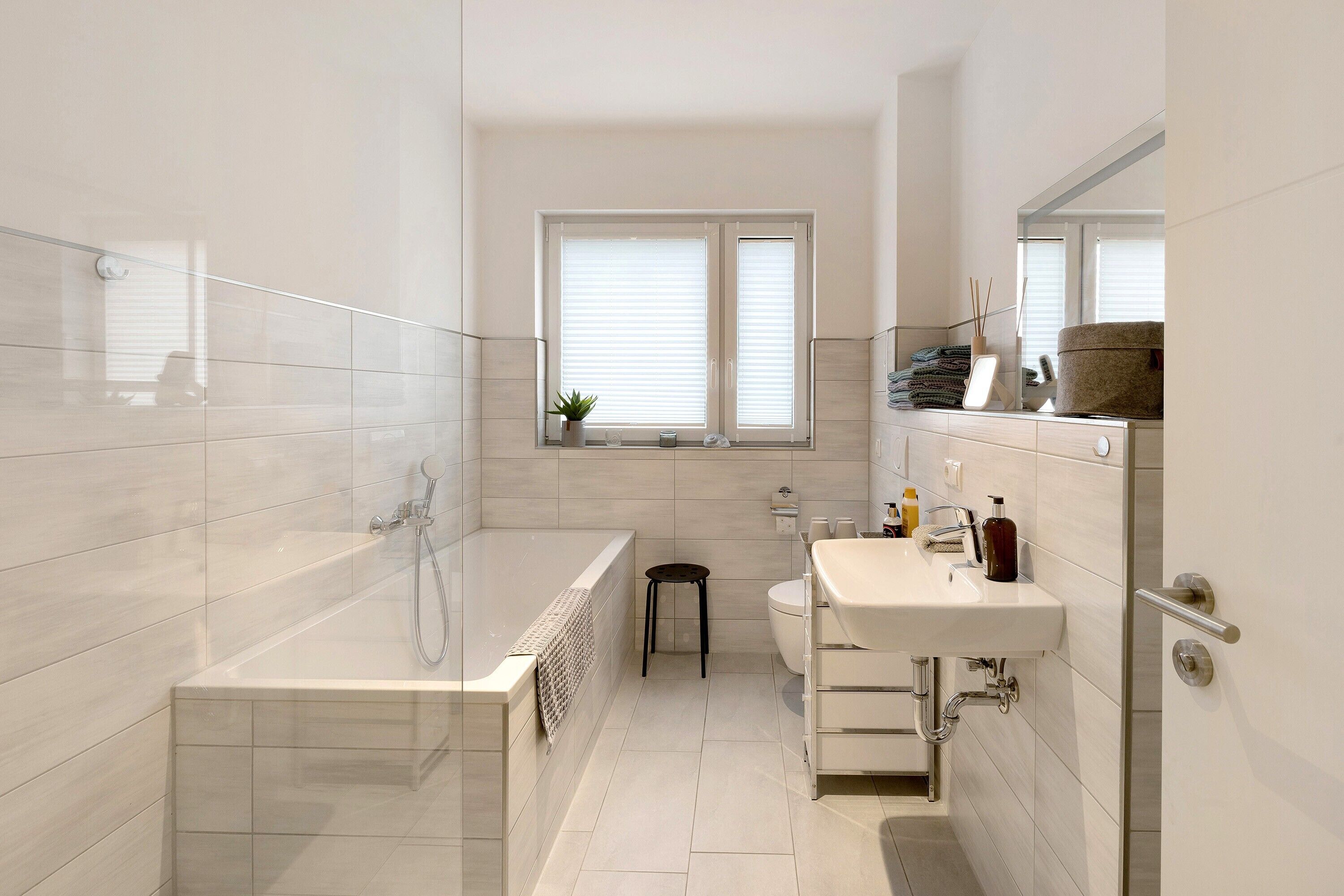 Een moderne badkamer met een bad, toilet, wastafel en een raam met zonwering.
