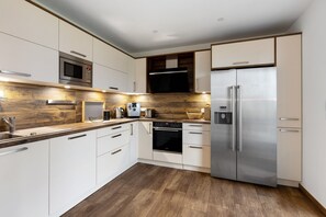 A modern kitchen with white cabinetry, stainless steel appliances, a wooden backsplash, and a built-in oven. - Apartment "Spanier" with Lake View, Private Terrace and Wi-Fi (Muldestausee OT Pouch)