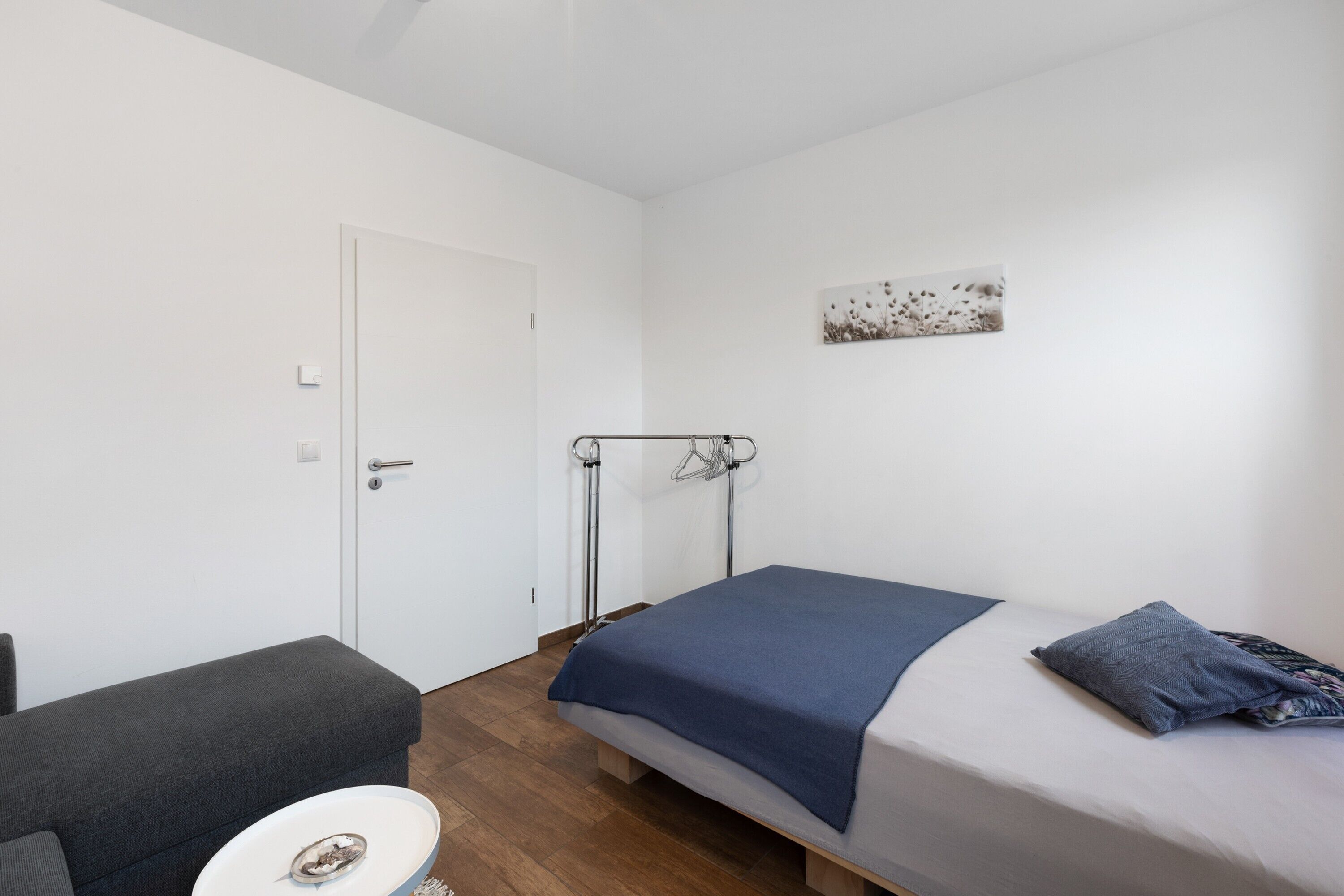 A bedroom with a bed, a bench, a small table, and a door.
