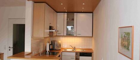 Una cocina compacta con armarios blancos, horno integrado, cafetera y lavabo.