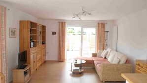 Ein Wohnzimmer mit einer Couch, einem Fernseher auf einem Schrank und einer Schiebetür zum Garten.