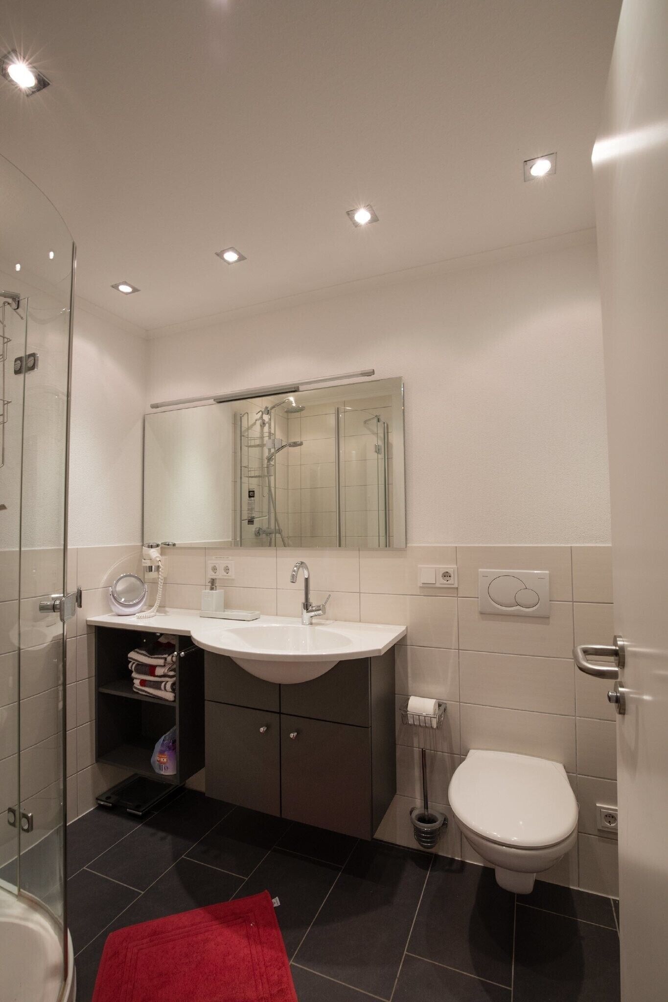Een moderne badkamer met een douchecabine van glas, een witte wastafel en een toilet.