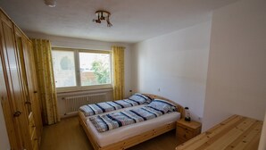 Ein Schlafzimmer mit einem hölzernen Bett, einem kleinen Nachttisch, einem Fenster mit Vorhängen und einer Heizung.