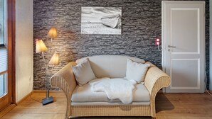 A room with a stone wall, a white door, a wicker sofa with a white throw blanket, and a lamp. - Apartment "Landharmonie Knüll" with Private Terrace, Balcony & Wi-Fi (Frielendorf)