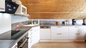 A modern kitchen with a wooden ceiling, white cabinets, a black induction cooktop, a microwave, and a coffee maker. - Apartment "Landharmonie Knüll" with Private Terrace, Balcony & Wi-Fi (Frielendorf)