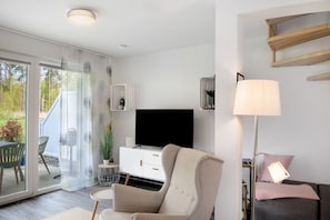 Un soggiorno moderno con una TV a schermo piatto, un divano, una poltrona, una lampada e una porta vetrata scorrevole che dà su uno spazio esterno.