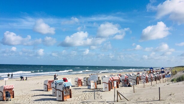 Une plage bordée de rangées de cabanes de plage et un ciel dégagé.