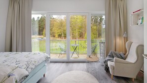 Une chambre à coucher comprenant un lit, une chaise, une petite table et un balcon avec vue sur les arbres.