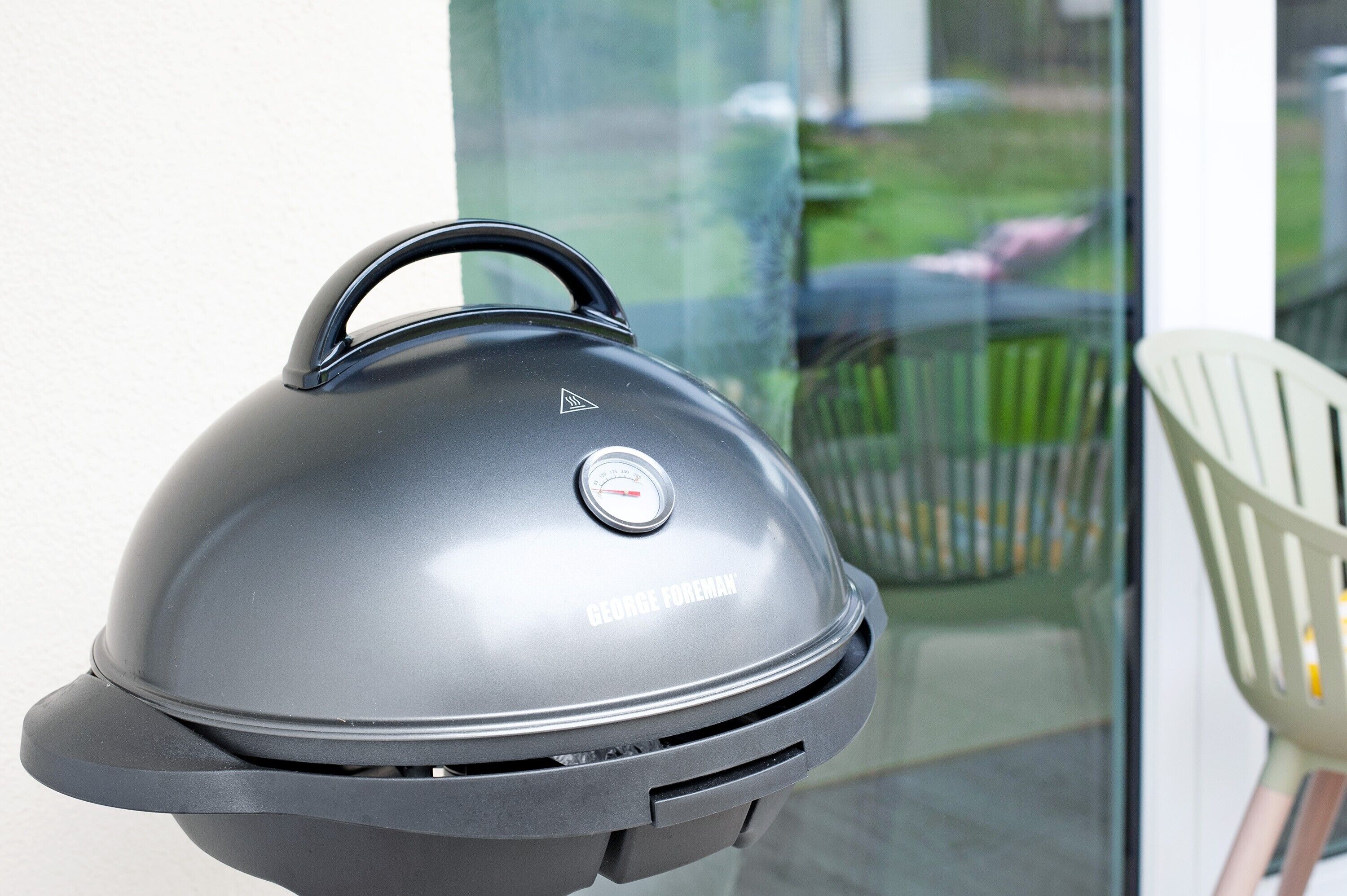 Una griglia George Foreman con termometro digitale, una porta in vetro e una sedia bianca sullo sfondo.