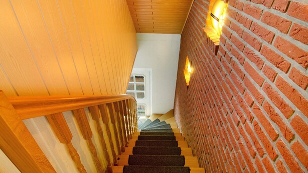 A wooden staircase with a brick wall on one side and a white wall on the other, leading to a door at the top.