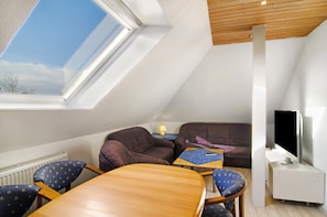 A room with a sloped ceiling, a television on a stand, a sofa, a table, and a chair.