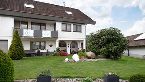 Une maison à deux étages dotée d’un balcon, d’une pelouse bien entretenue et de diverses plantes.