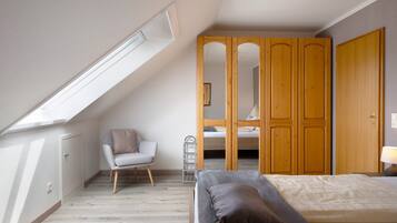 A bedroom with a sloped ceiling, a bed, a chair, a wardrobe, and a mirror.