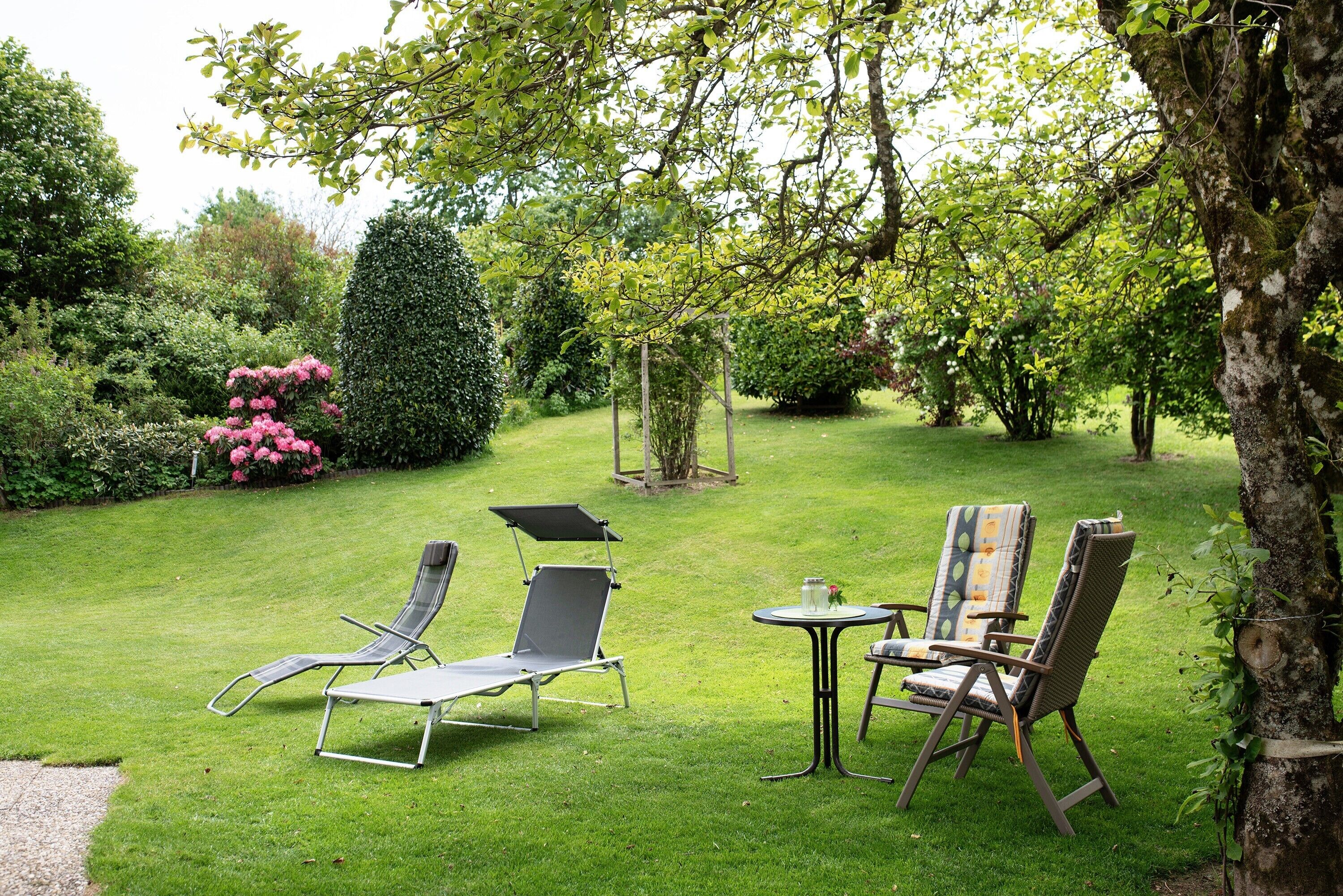 A garden with a lawn, two lounge chairs, a small table, and a swing.