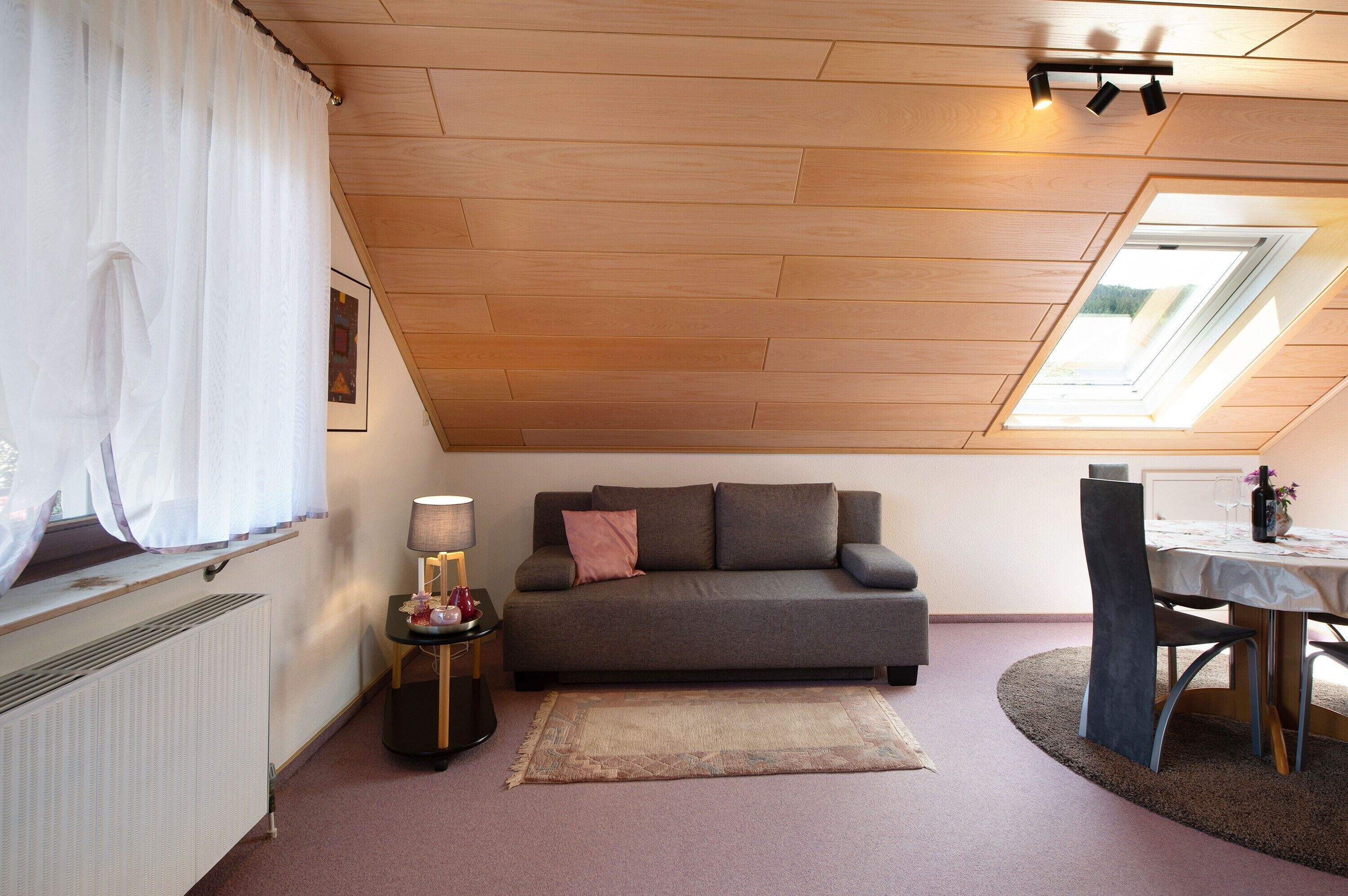 A room with a sloped ceiling, a sofa, a table, and a window with a view.