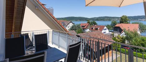 A balcony with a table and chairs, overlooking a lake with houses and a clear sky.