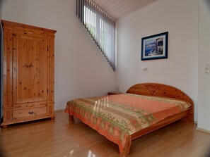 Un dormitorio con una cama de madera, un armario, una escalera y un cuadro enmarcado en la pared.