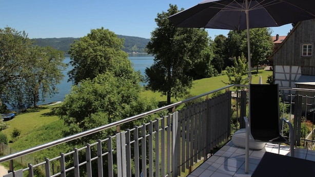 A balcony with a view of a lake, a wooden house, and a metal railing. - Apartment '1 O G' with Lake View, Balcony and Wi-Fi (Bodman-Ludwigshafen)